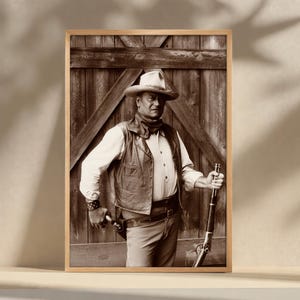 Peut inclure: Impression encadrée en sépia d'un cow-boy avec un chapeau, un gilet et une écharpe, tenant un fusil et un pistolet. Le cow-boy se tient devant une porte en bois. L'image est dans un cadre en bois.