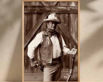 May include: Sepia-toned framed print of a cowboy in a hat, vest, and scarf, holding a rifle and a pistol. The cowboy stands in front of a wooden door. The image is in a wooden frame.