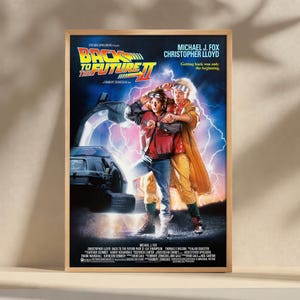 Puede incluir: Un póster enmarcado de la película "Regreso al Futuro Parte II" con Michael J. Fox y Christopher Lloyd. El póster tiene un fondo azul oscuro con el título en amarillo y rojo, y los actores están en primer plano.