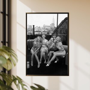 K&ouml;nnte beinhalten: Schwarz-wei&szlig; gerahmtes Foto von f&uuml;nf lachenden Frauen auf einem Dach. Die Frauen tragen Kleider und Shorts. Die Skyline von New York ist im Hintergrund zu sehen.
