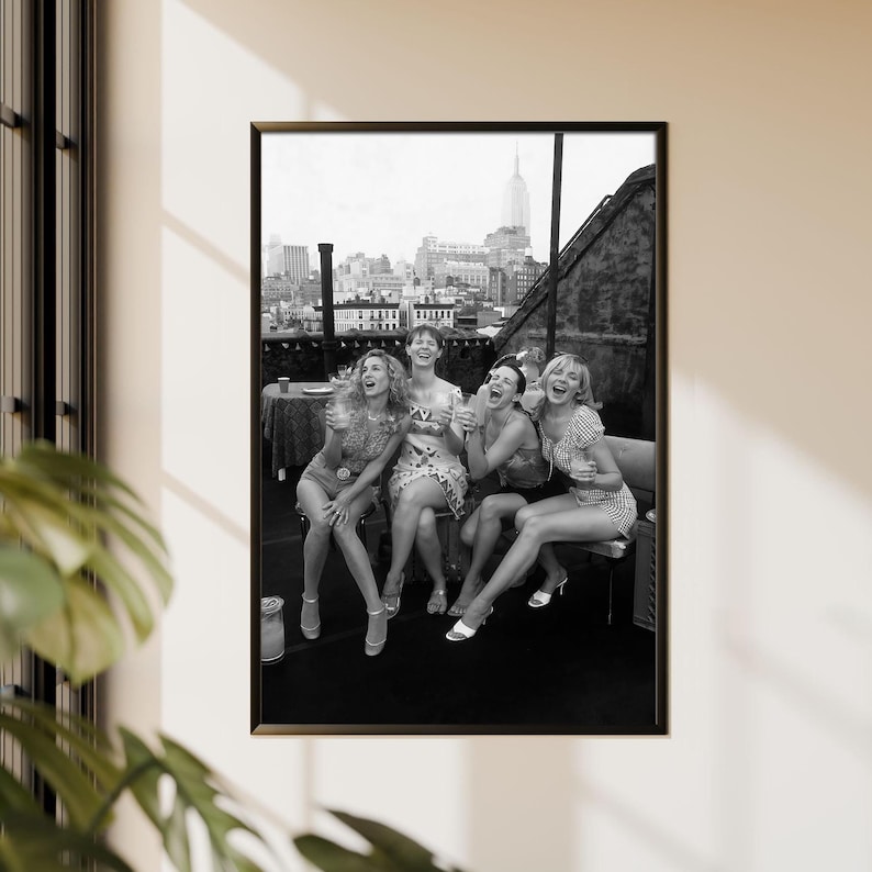 K&ouml;nnte beinhalten: Schwarz-wei&szlig; gerahmtes Foto von f&uuml;nf lachenden Frauen auf einem Dach. Die Frauen tragen Kleider und Shorts. Die Skyline von New York ist im Hintergrund zu sehen.
