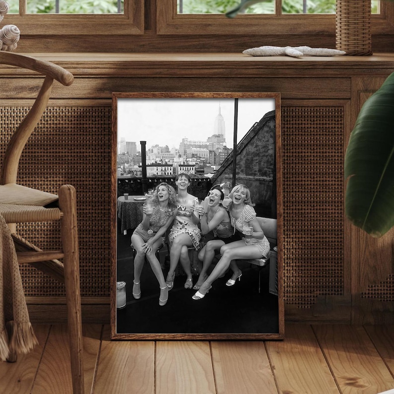K&ouml;nnte beinhalten: Schwarz-wei&szlig; gerahmtes Foto von f&uuml;nf lachenden Frauen auf einem Dach mit Skyline im Hintergrund. Die Frauen tragen Kleider und Abs&auml;tze und sitzen auf einer Bank.