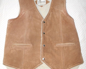 May include: A brown suede vest with a cream-colored, fuzzy lining and three dark buttons. The vest has two front pockets and a label near the collar. The vest is a classic style.