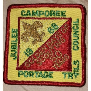 Puede incluir: Un parche cuadrado bordado con fondo amarillo y borde rojo. El parche presenta texto que dice "Camporee", "Jubilee", "Portage", "Council" y "Vils Try". También hay un emblema dorado y los números "68" y "69".