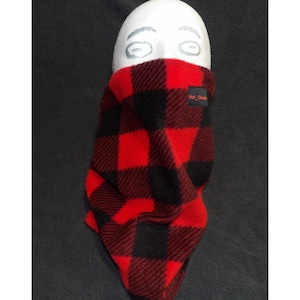 May include: Red and black plaid fleece neck warmer. The neck warmer is wrapped around a white mannequin head. The tag on the neck warmer reads "Hot Cheeks".
