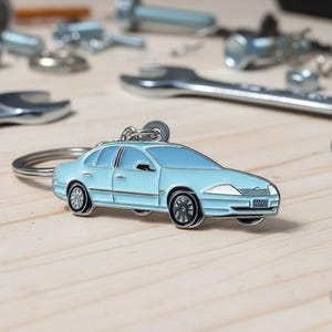 May include: A light blue car keyring with black wheels and silver trim. The keyring is on a silver ring. The background includes various silver tools, such as spanners and bolts, on a light wooden surface.