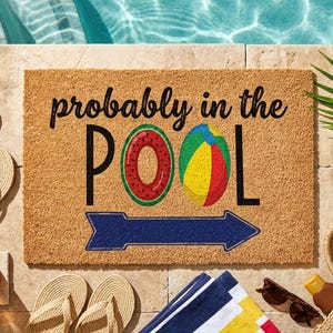 Puede incluir: Una alfombra rectangular con el texto "probably in the POOL" y un diseño de sandía y pelota de playa. La alfombra está junto a una piscina, con chanclas, una bebida y una bolsa de playa.