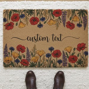 Könnte beinhalten: Eine rechteckige Fußmatte mit floralem Design mit roten Mohnblumen, gelben Blumen, blauen Kornblumen und lila Lupinen. Der Text "custom text" ist in einer Schrift geschrieben. Die Matte liegt auf einem weißen Teppich.