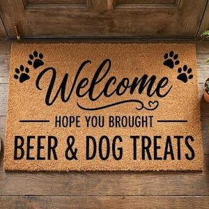 Può includere: Un zerbino rettangolare con la scritta "Welcome" in corsivo, accompagnata da impronte di zampe. Il testo "HOPE YOU BROUGHT BEER & DOG TREATS" è sotto. Due paia di scarpe da ginnastica sono sul pavimento di legno.