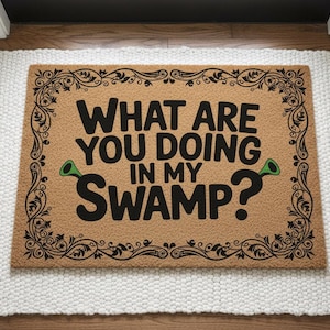 Peut inclure: Un paillasson rectangulaire avec l'inscription "WHAT ARE YOU DOING IN MY SWAMP ?" en lettres noires. Le paillasson a un fond marron avec une bordure noire décorative et des accents verts. Il repose sur un tapis blanc.