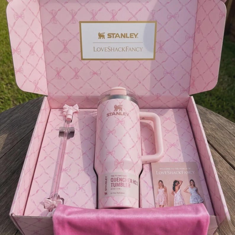 May include: A pink Stanley Quencher H2.0 Flowstate tumbler with a handle, bow pattern, and a clear lid, inside a matching pink box. The box includes a pink straw and a small card. The tumbler is 1.18 liters.