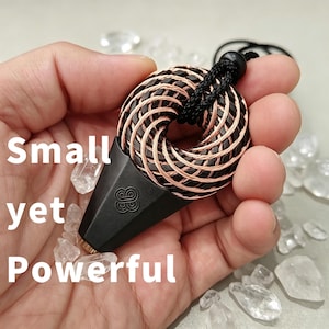 May include: A pendant featuring a circular, braided copper wire coil attached to a matte black, triangular base with a small embossed logo. The piece is suspended from a black cord and includes the text Small yet Powerful printed on the image.