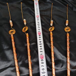 以下が含まれることがあります： 銅線で巻かれた4本の銅棒。それぞれの上部には渦巻き模様と小さな透明なクリスタルポイントがあしらわれています。銅棒の間には白いメジャーが置かれており、長さが約50cmであることを示しています。