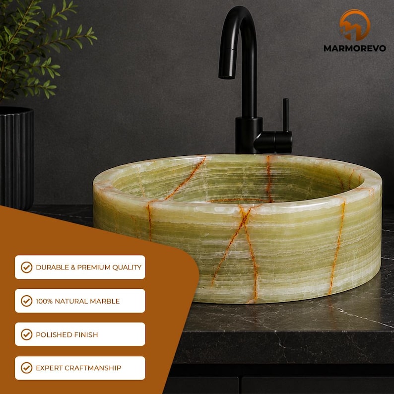 May include: A round, light green marble vessel sink featuring prominent orange-brown veining throughout its polished surface. A matte black faucet is positioned behind the sink. The text MARMOREVO appears in the top right corner.