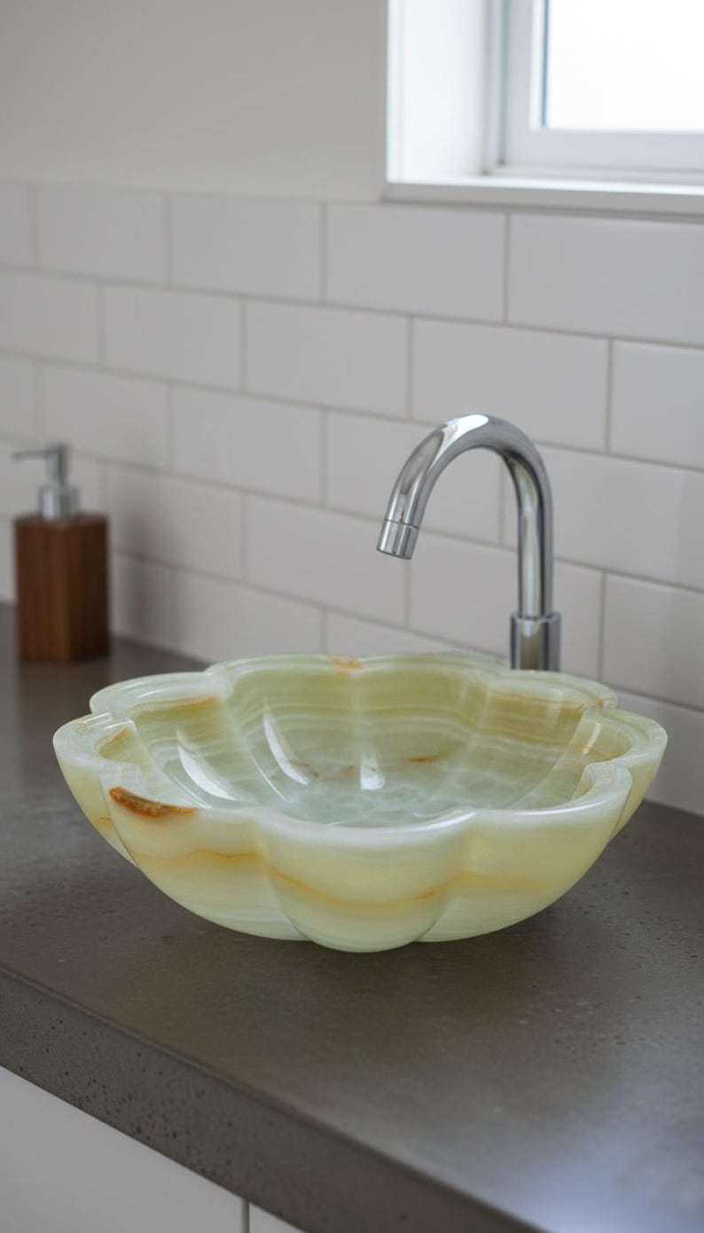 May include: A flower-shaped vessel sink carved from pale green and translucent white onyx stone with natural golden-brown veining. The basin features a scalloped rim and a smooth, polished finish, paired with a curved chrome faucet.