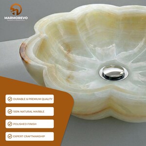 May include: A flower-shaped bathroom sink carved from translucent light green and cream-colored natural marble with a polished finish and a centered chrome drain. The text MARMOREVO MARBLE & HANDICRAFTS appears in the upper left corner.