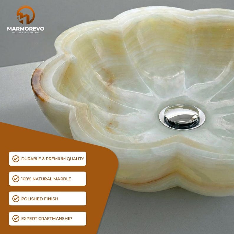 May include: A flower-shaped bathroom sink carved from translucent light green and cream-colored natural marble with a polished finish and a centered chrome drain. The text MARMOREVO MARBLE & HANDICRAFTS appears in the upper left corner.