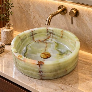 May include: A round vessel sink crafted from polished green onyx stone with natural brown veining. The sink features a matching stone drain cover and is paired with a wall-mounted brushed gold faucet and a single lever handle control.