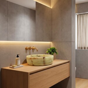 May include: A round, light green onyx vessel sink with natural brown veining sits atop a light wood floating vanity. A wall-mounted brass tap is positioned above the sink, accompanied by a soap dispenser and a small green plant.