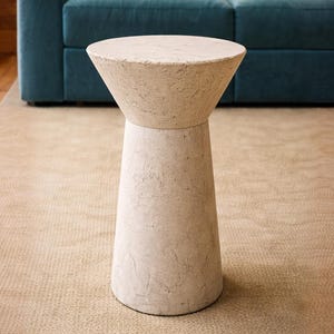 Könnte beinhalten: Ein beiger, moderner Beistelltisch mit konischer Oberseite und zylindrischem Sockel. Der Tisch besteht aus einem strukturierten, hellfarbigen Material und ist etwa 51 cm hoch. Der Tisch steht auf einem neutralfarbenen Teppich.