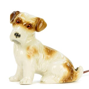 Könnte beinhalten: Eine sitzende Hunde-Figur aus Keramik mit weißem Grund und braunen Markierungen und Akzenten. Der Hund hat braune Ohren und bernsteinfarbene Augen. Ein braunes Elektrokabel ragt aus der Basis der Figur heraus.