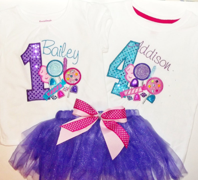 Puede incluir: Dos camisetas blancas con n&uacute;meros morados y azules, caramelos y los nombres Bailey y Addison. Un tut&uacute; de tul morado con un lazo rosa de lunares blancos.