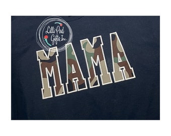 May include: A navy blue t-shirt with a white outline of the word "MAMA" in a camouflage pattern.