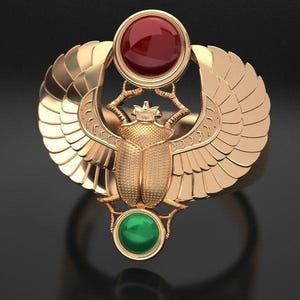 Pode incluir: Anel dourado com um design de besouro escaravelho com asas abertas. O anel tem uma pedra preciosa vermelha no topo e uma pedra preciosa verde na parte inferior. O anel está sobre um fundo escuro.