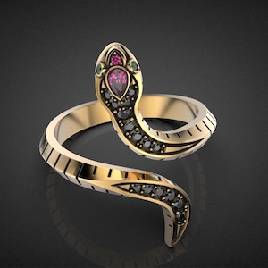 May include: A gold-colored snake ring with a detailed design. The snake's head features a teardrop-shaped pink gemstone, with smaller green and black gemstones. The ring's body is adorned with black gemstones and geometric patterns.