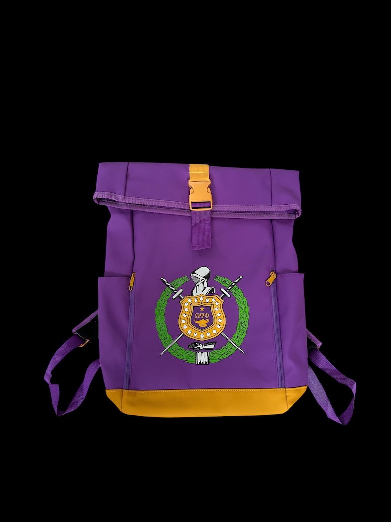 May include: Purple backpack with a yellow accent at the bottom and a yellow buckle. The front of the backpack features a crest with a knight, swords, and a wreath. The backpack has two side pockets with yellow zippers.