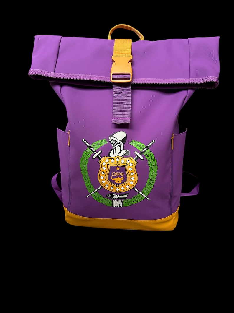 May include: Purple backpack with a yellow buckle and accents. The front features a crest with crossed swords, a wreath, and the Greek letters Omega, Upsilon, and Phi. The bottom of the backpack is yellow.
