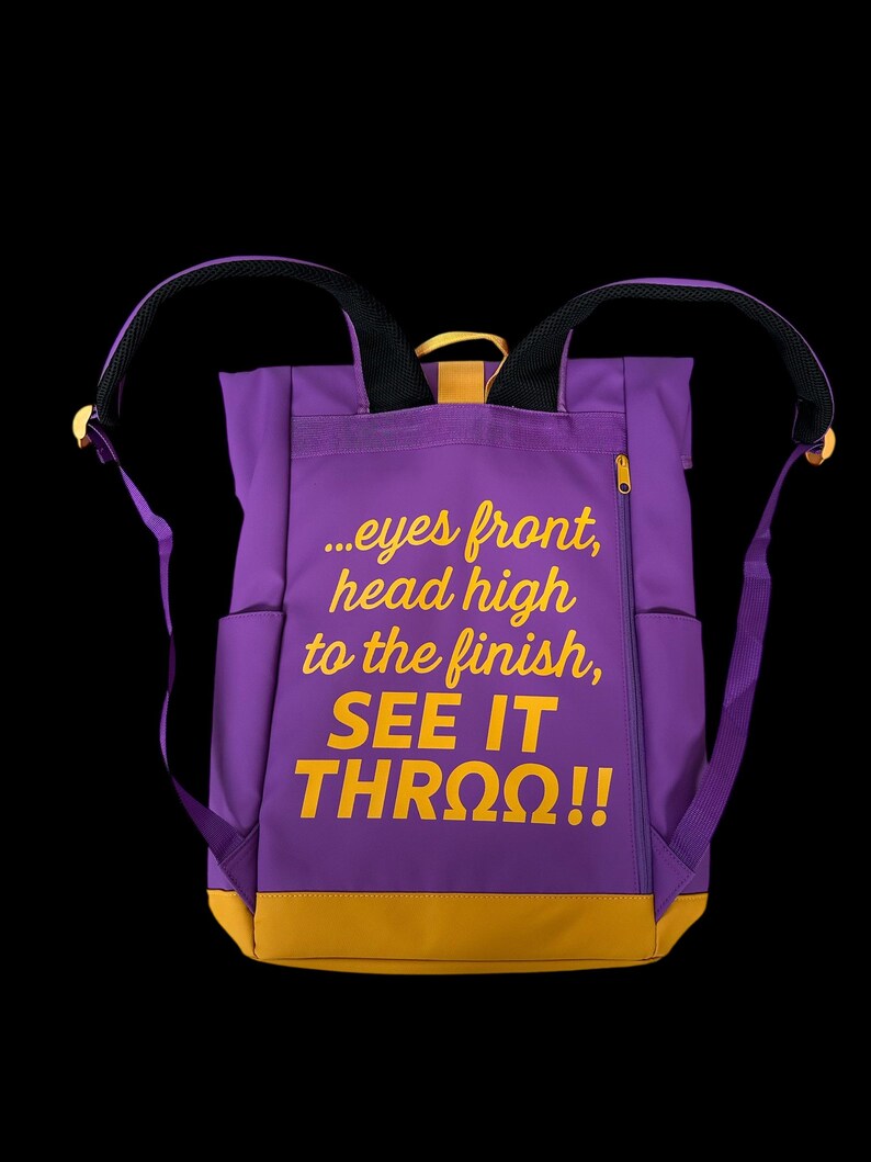 May include: Purple backpack with yellow accents and the text "...eyes front, head high to the finish, SEE IT THRO&Omega;!!" The backpack has two side pockets, a zippered front pocket, and adjustable straps.