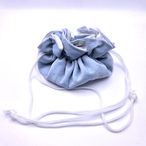 Puede incluir: Una bolsa de cordón de ante azul claro con interior blanco. La bolsa se frunce en la parte superior con un cordón blanco. La bolsa está sobre un fondo blanco.