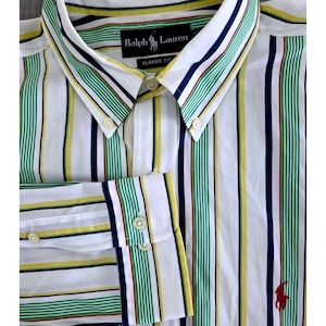 May include: White button-down shirt with vertical stripes in green, yellow, and navy blue. The shirt features a classic fit and the Ralph Lauren logo in red. The cuff and collar are also striped.