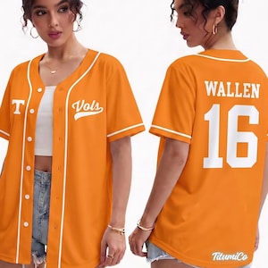 Puede incluir: Camiseta de béisbol naranja con ribetes y botones blancos. La camiseta tiene la letra "T" y la palabra "Vols" en la parte delantera. La parte trasera de la camiseta muestra el nombre "WALLEN" y el número "16" en blanco.