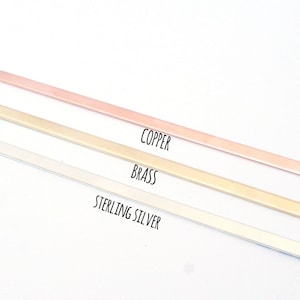 May include: Three metal strips in different colors: copper, brass, and sterling silver. The strips are arranged vertically, with the copper strip at the top and the sterling silver strip at the bottom.