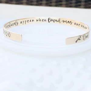 May include: A gold-toned bangle bracelet with the inscription "Cardinals appear when loved ones are near 2020" and a small bird design.