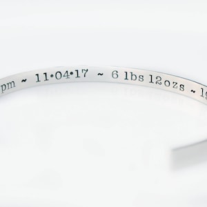 May include: Silver bangle bracelet with an engraved inscription: "8:39 pm ~ 11.04.17 ~ 6 lbs 12 ozs ~ 19.5"