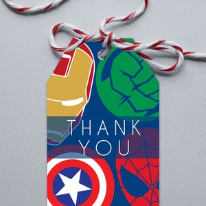Peut inclure: Une étiquette cadeau rectangulaire avec un fond bleu et l'inscription "THANK YOU" en blanc. L'étiquette présente des illustrations d'emblèmes de super-héros, dont Iron Man, Hulk, Captain America et Spider-Man. Une ficelle rouge et blanche est attachée.