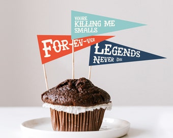 Könnte beinhalten: Ein Schokoladen-Cupcake auf einem weißen Teller, verziert mit drei Wimpelfahnen. Die Fahnen sind rot, türkis und marineblau, mit weißem Text, der "FOREVER", "YOU'RE KILLING ME SMALLS" und "LEGENDS NEVER DIE" lautet.