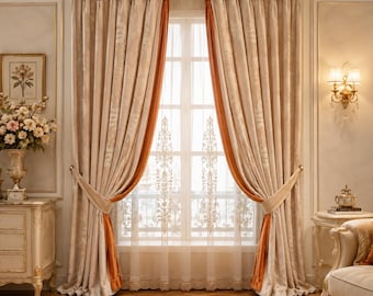 May include: Floor-length curtains featuring a beige damask pattern with solid burnt orange side panels. The curtains are hung on a gold-toned rod with pleated headers and are tied back to reveal a sheer white lace panel with vertical floral motifs.