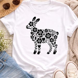 Peut inclure: T-shirt blanc avec un motif de lapin floral noir. La silhouette du lapin est remplie de diverses formes de fleurs et de feuilles. Le t-shirt est présenté avec un short en jean, un chapeau de paille, des lunettes de soleil et des baskets blanches.