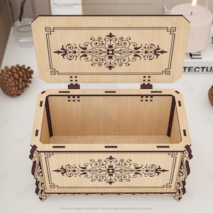 May include: Open wooden box with a hinged lid, featuring intricate dark brown floral and geometric designs. The box is light brown with dark brown accents and is open, revealing the interior. Decorative and ornate.
