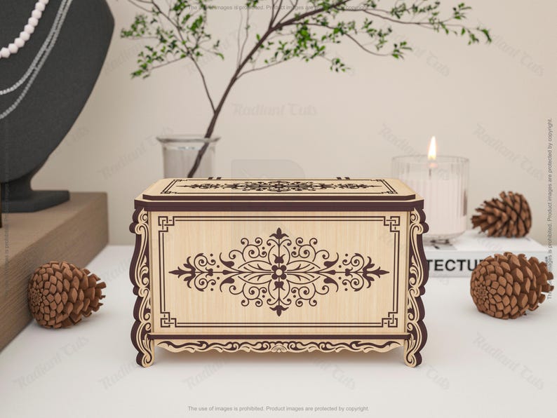 May include: A decorative wooden box with intricate floral and scrollwork designs. The box is light-colored with dark brown accents and a rectangular shape. The design is symmetrical and features a central floral motif. The box is displayed with pinecones and a candle.