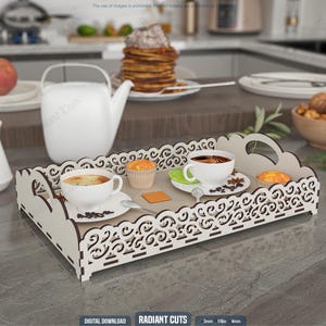 Peut inclure: Un plateau de service décoratif en bois avec un motif ajouré blanc, contenant deux tasses de café, deux muffins et un petit carré de beurre. Un pot à thé et une crème blanche sont à l'arrière-plan. Le plateau mesure environ 30 cm de long.