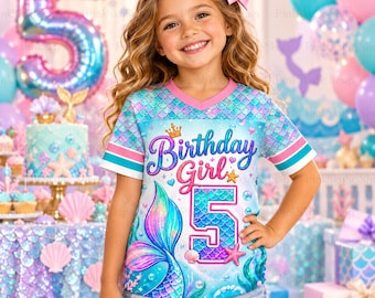 May include: A short-sleeve V-neck t-shirt featuring a mermaid-themed graphic with the text Birthday Girl and the number 5. The shirt has a blue and pink scale pattern, a mermaid tail illustration, and pink and blue striped sleeve cuffs.