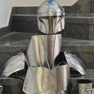 May include: A complete set of polished silver armor, including a helmet, chest plate, shoulder guards, and leg pieces. The helmet has a distinctive T-shaped visor. The armor is displayed on a set of stairs.
