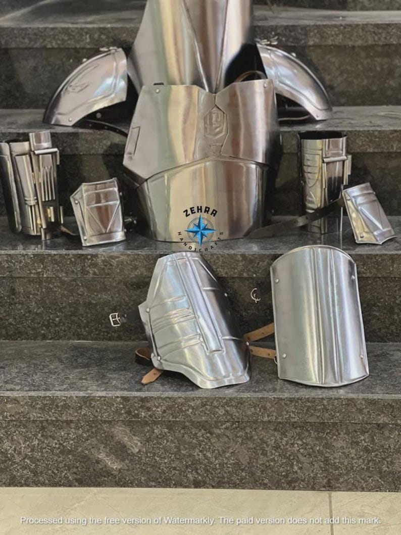 May include: A collection of polished silver metal armor pieces, including a chest plate, shoulder guards, and arm and leg protection. The armor is displayed on a set of gray steps. The text "ZEHRA HANDICRAFTS" is visible.