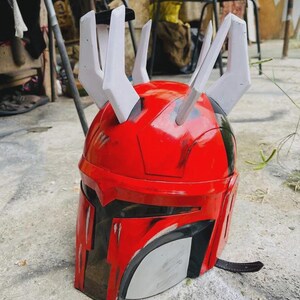 May include: A red and black helmet with white horns. The helmet has a visor and a chin strap. The helmet is likely a costume or prop.