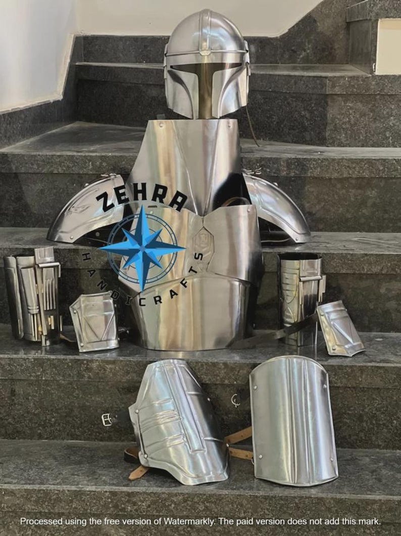 May include: A complete set of metallic silver Mandalorian armor, including a helmet, chest plate, shoulder pads, and various other protective pieces. The armor is displayed on a set of gray steps. The text "ZEHRA HANDICRAFTS" is visible.